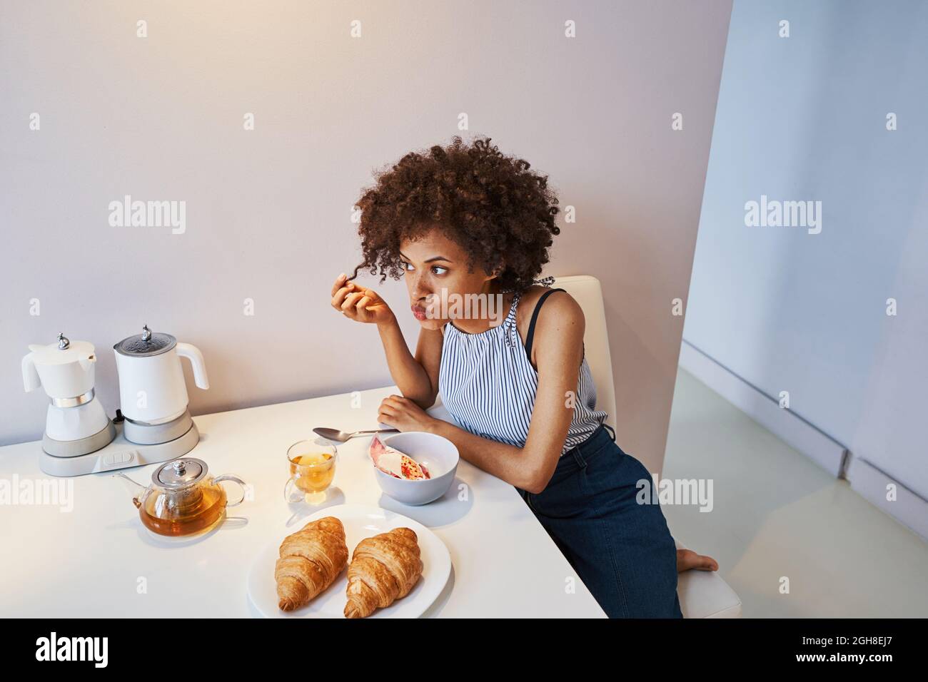 Nette, lockige Dame, die sich beim Frühstück gelangweilt fühlt Stockfoto