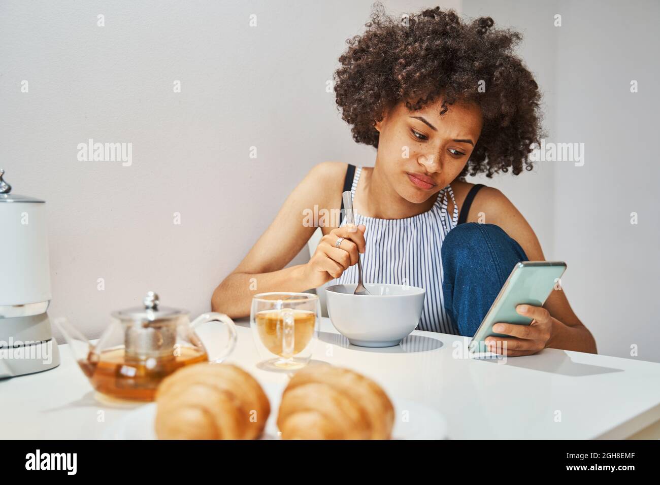 Nette junge Frau, die beim Frühstück eine SMS liest Stockfoto