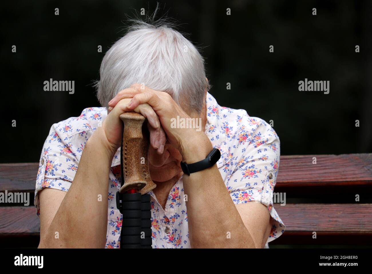 Ältere Frau, die mit dem Kopf nach unten auf Spazierstöcken auf einer Bank sitzt. Krankheit und Müdigkeit, gesunder Lebensstil im Alter, Leben im Ruhestand Stockfoto