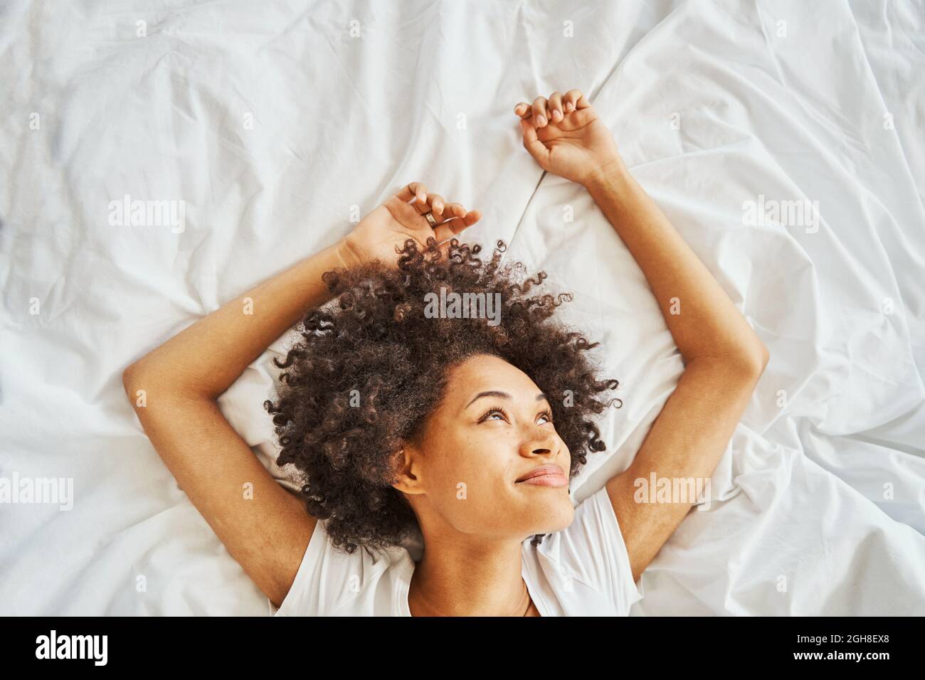 Nette Dame mit dicken dunklen lockigen Haaren Tagträumen im Bett Stockfoto