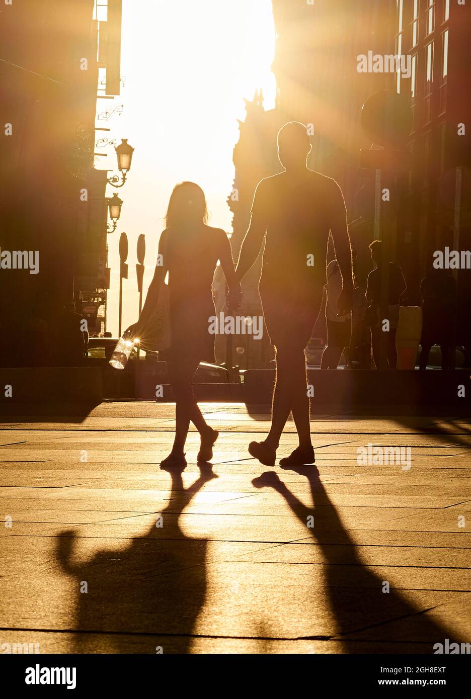 Silhouette eines jungen Paares, das die Hände auf einer warmen Straße vor einem Hintergrund in der Dämmerung hält. Stockfoto