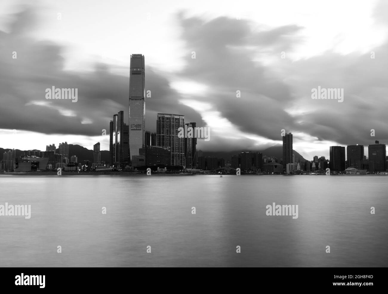 Schwarzweiß-Foto von Hong Kong Island mit Blick über den Victoria Harbour nach Kowloon und den ICC-Wolkenkratzer. Lange Exposition gibt seidiges Meer. Stockfoto