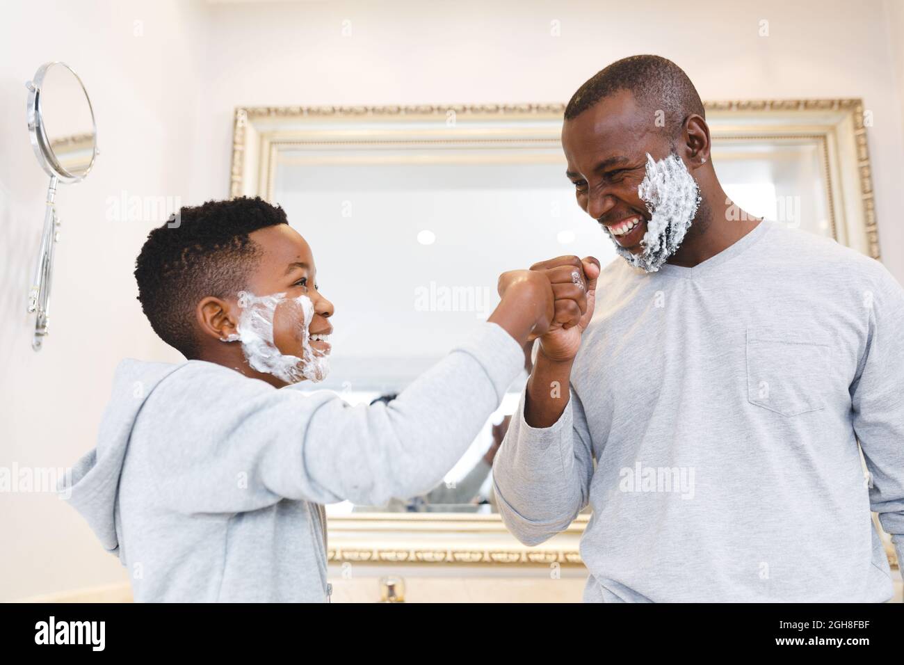 afroamerikanischer Vater mit Sohn, der Spaß mit Rasierschaum hat, und im Badezimmer die Fäuste anstößt Stockfoto