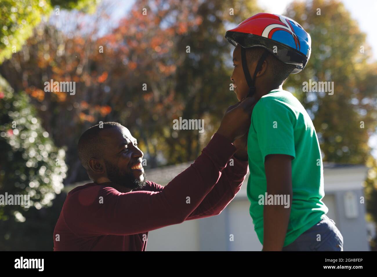 afroamerikanischer Vater mit Sohn lächelt und bereitet sich vor dem Skateboarden im Garten vor Stockfoto