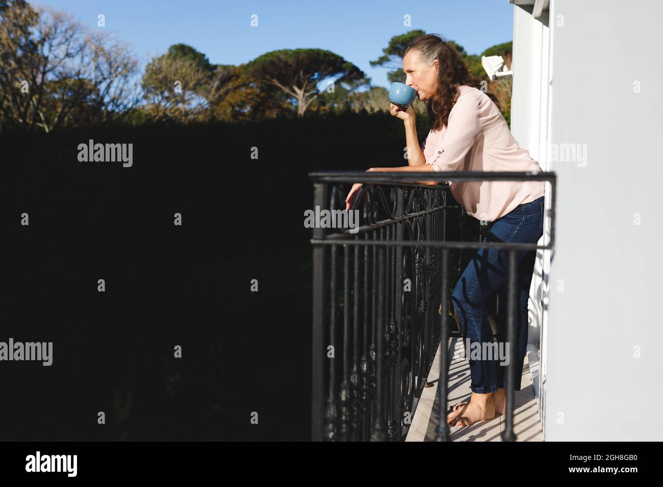 Glückliche ältere kaukasische Frau, die Kaffee trinkt und auf dem Balkon steht Stockfoto