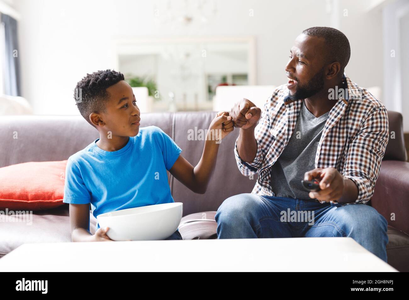 Glücklicher afroamerikanischer Vater und Sohn sitzen auf dem Sofa und stoßen mit der Faust vor dem fernseher Stockfoto