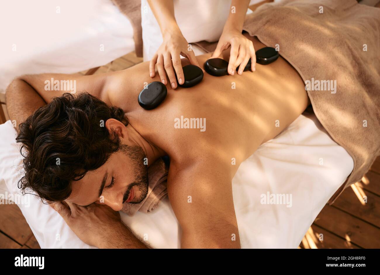 Der gutaussehende Mann im Spa Resort erhält eine Hot Stone Massage. Massagetherapie mit heißen Steinen mit glatten, flachen, beheizten Steinen Stockfoto