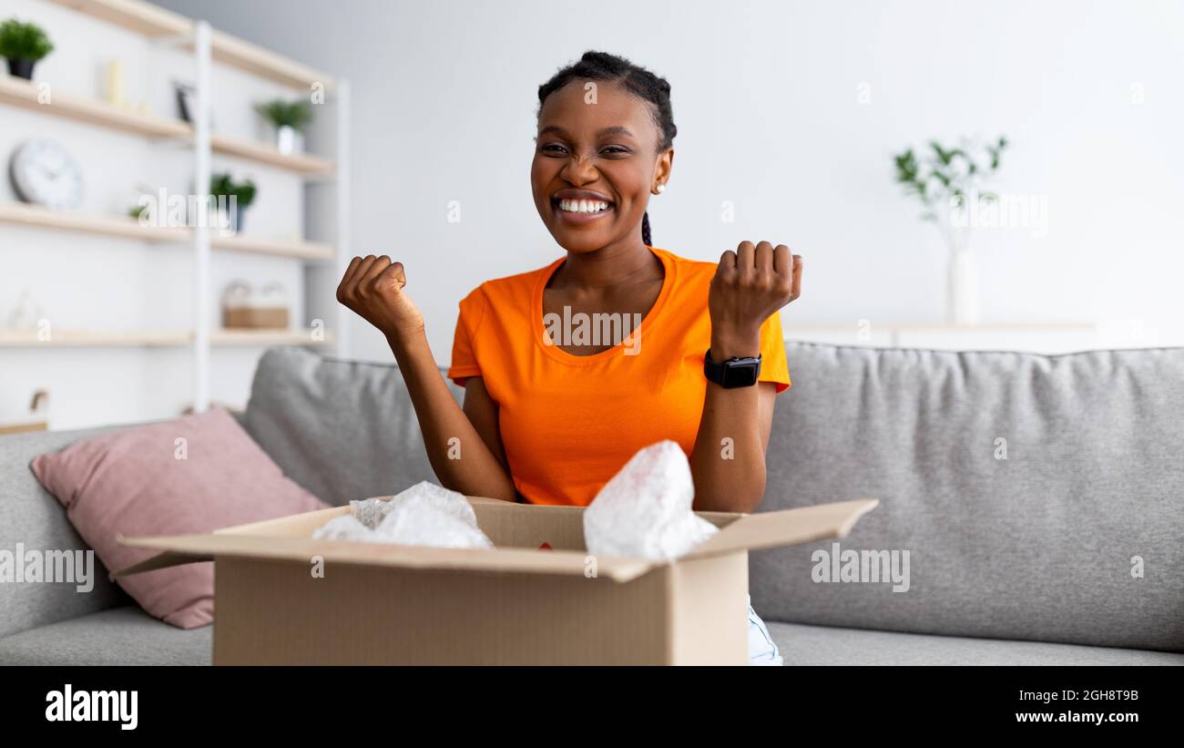 Banner für Online-Shopping und -Lieferung. Aufgeregt schwarze Frau, die zu Hause das Paket öffnet, gestikuliert JA, zufrieden mit dem Service Stockfoto