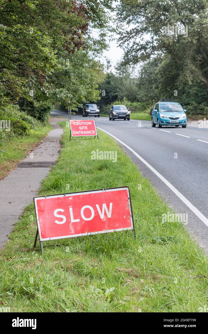 Rotes SLOW-Zeichen auf einer Landstraße in Cornwall (Fokus auf Slow). Für Straßenbauarbeiten UK, UK Straßenschilder, Verkehrsmanagement, gehen langsam Zeichen. Stockfoto