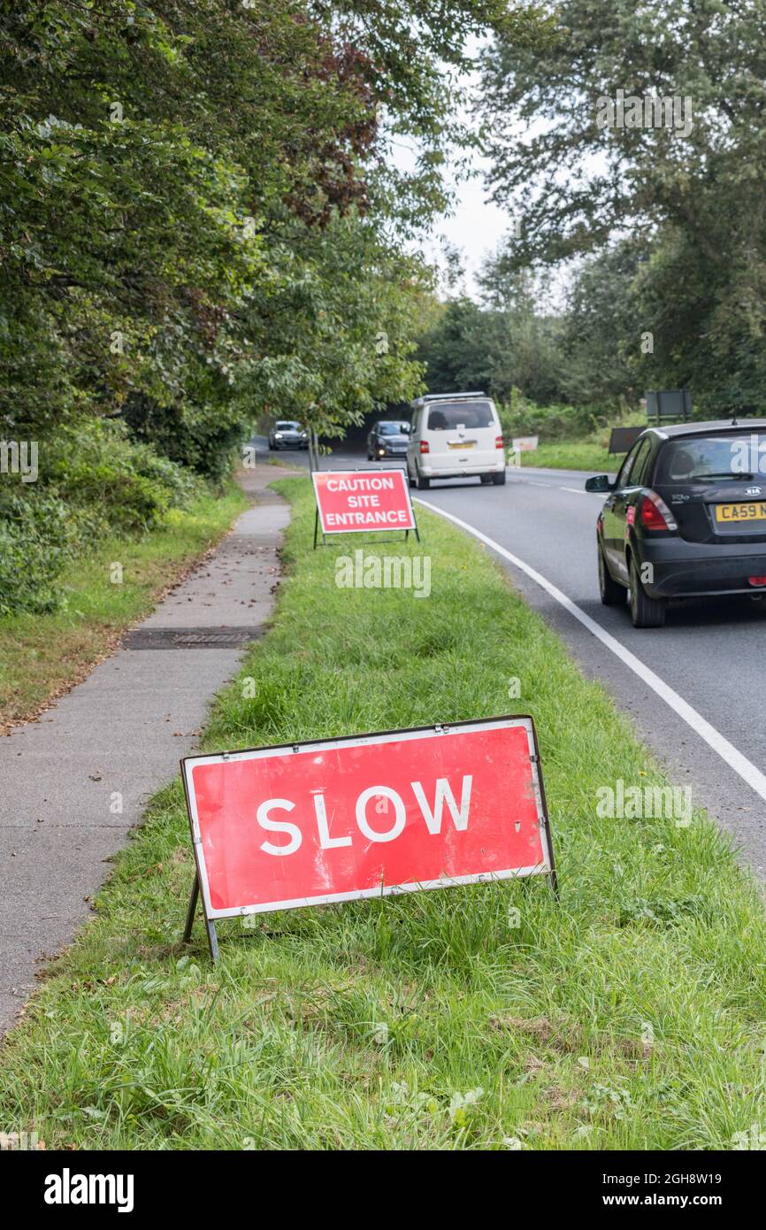 Rotes SLOW-Zeichen auf einer Landstraße in Cornwall (Fokus auf Slow). Für Straßenbauarbeiten UK, UK Straßenschilder, Verkehrsmanagement, gehen langsam Zeichen. Stockfoto
