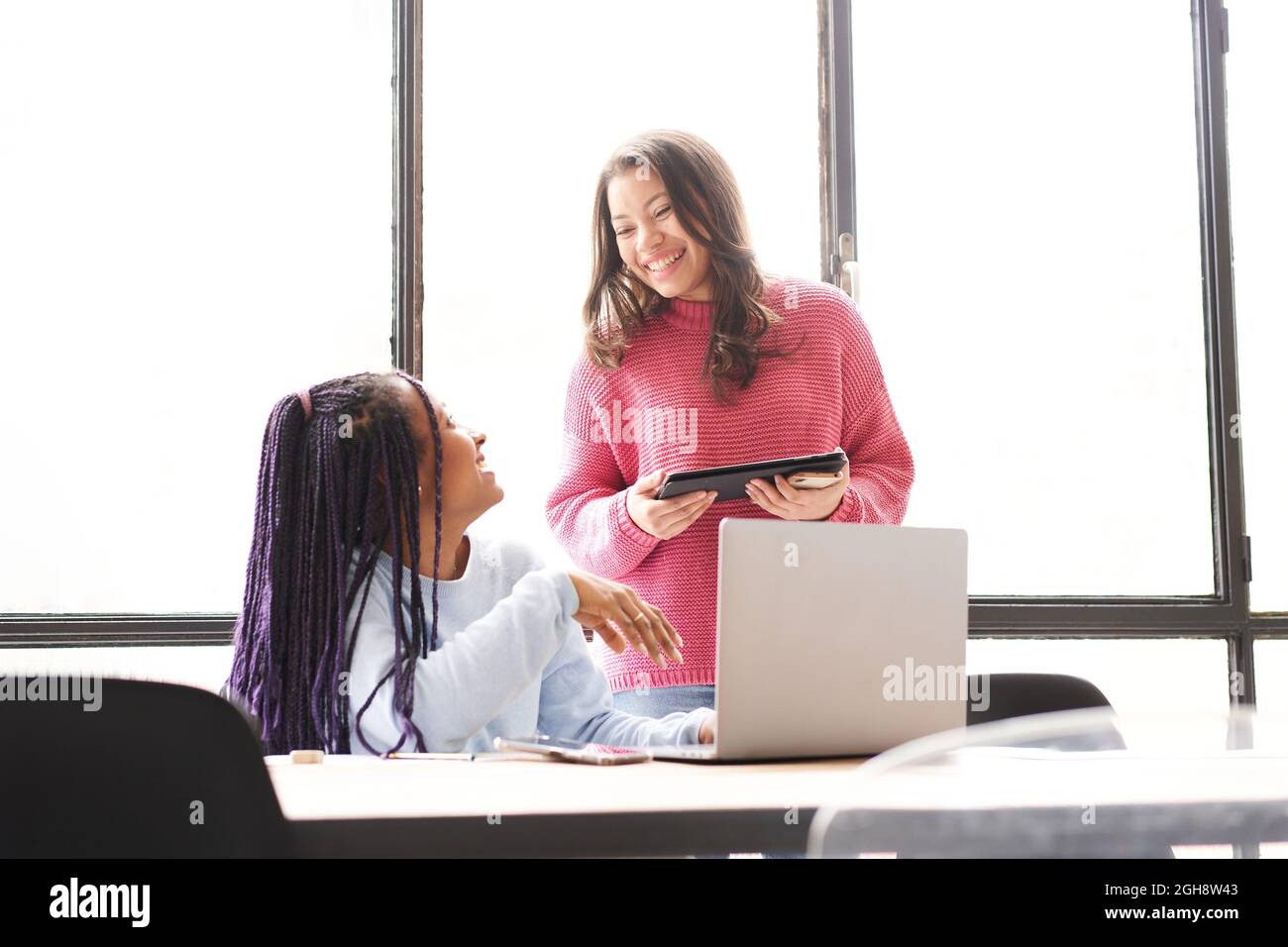 Im Büro: Zwei Frauen arbeiten zusammen. Sie diskutieren Arbeitsprobleme freundlich, während sie auf den Computerbildschirm schauen. Stockfoto