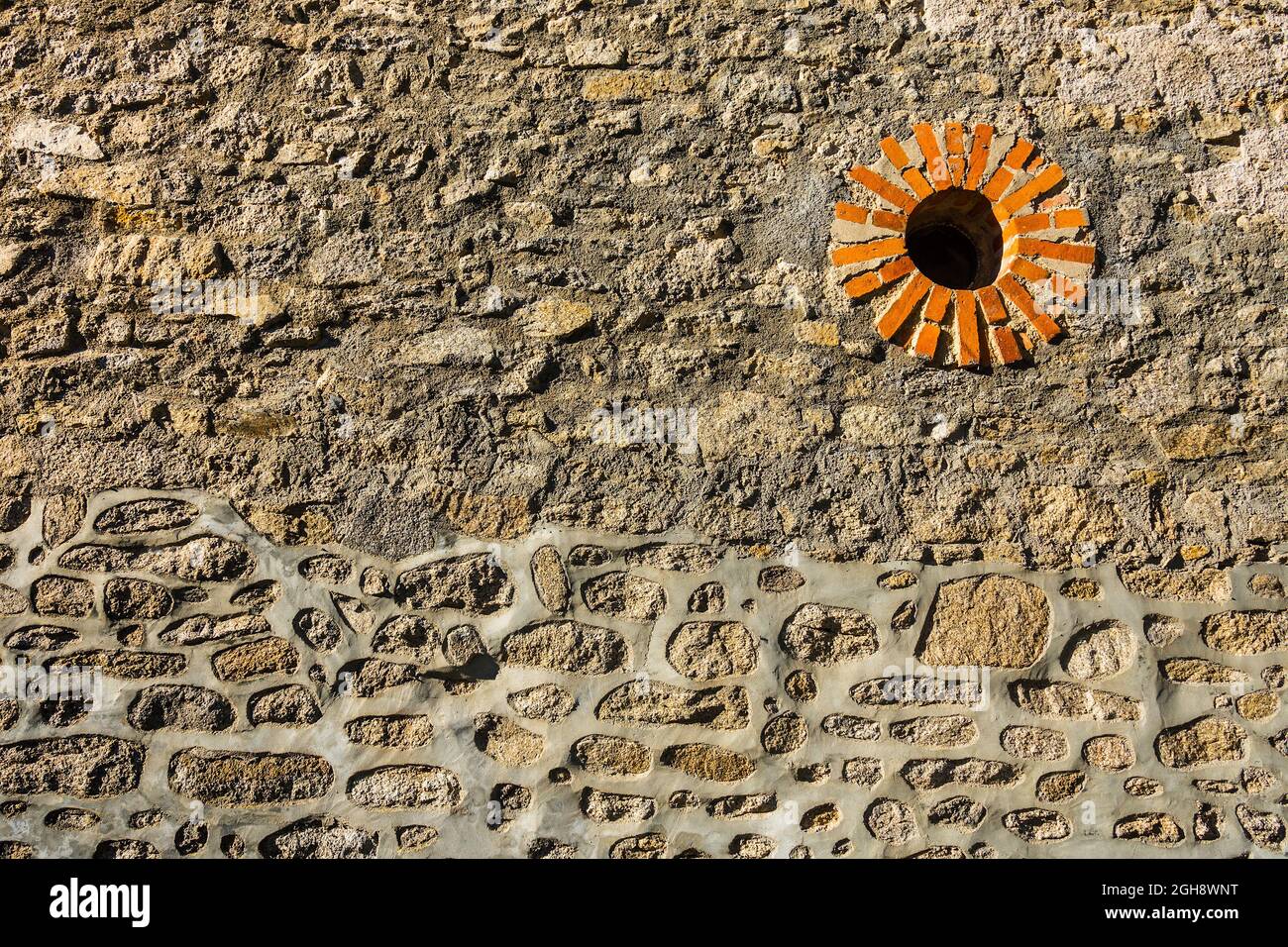 Alte zufällige Granitsteinmauer mit rundem Ziegelfenster - Bénévent-l'Abbaye, Creuse (23), Nouvelle-Aquitaine, Frankreich. Stockfoto