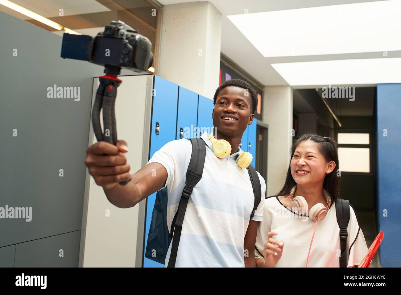 Interrassisches Studentenpaar, das ein Video für soziale Medien macht. Selfie von zwei jungen Menschen, die in der High School mit einer Videokamera Selfie machen. Vlogging. Stockfoto