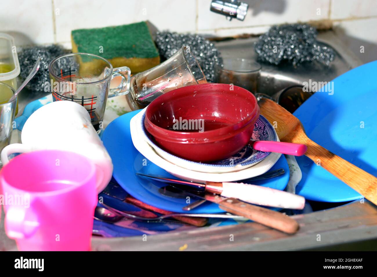 Ungewaschene Küchenutensilien im Waschbecken müssen gereinigt und gewaschen werden, ein Haufen schmutziges Geschirr, Messer, Töpfe und Trinkglas im Spülbecken Stockfoto