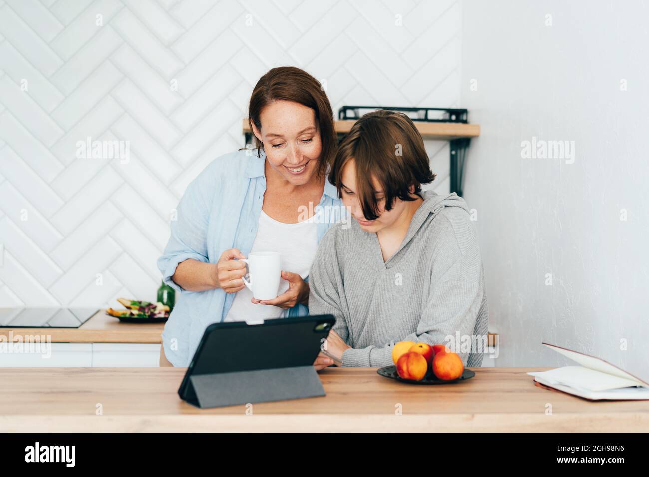 Mutter und Tochter im Teenageralter in der Küche beobachten ein soziales Netzwerk am Telefon und haben Spaß. Stockfoto