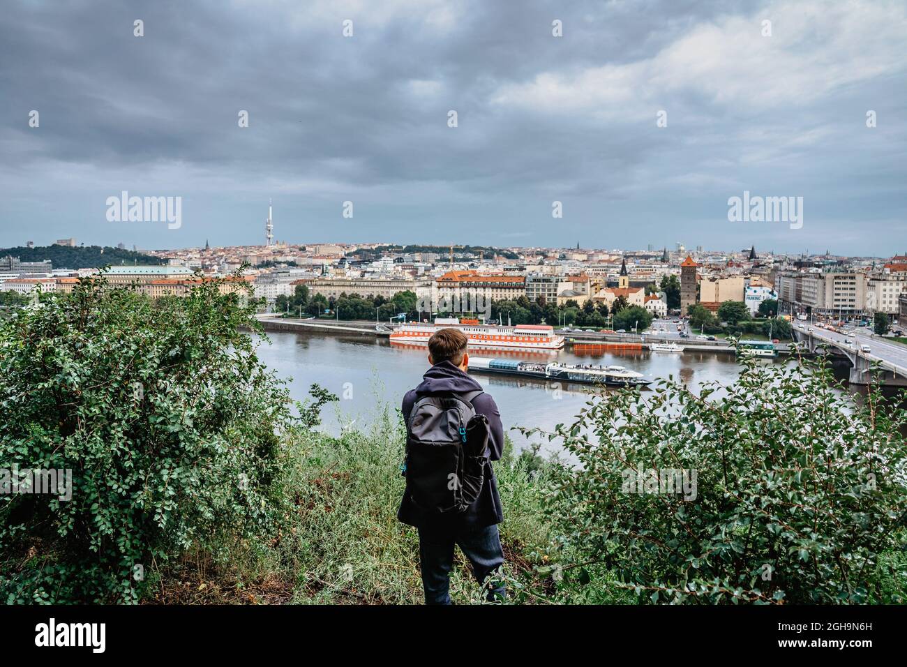 Junger männlicher Rucksacktourist, der die Aussicht auf die Prager Skyline und den Fluss Moldau vom Letna Park, Tschechische Republik, genießt.Prag Panorama am bewölkten regnerischen Tag Stockfoto