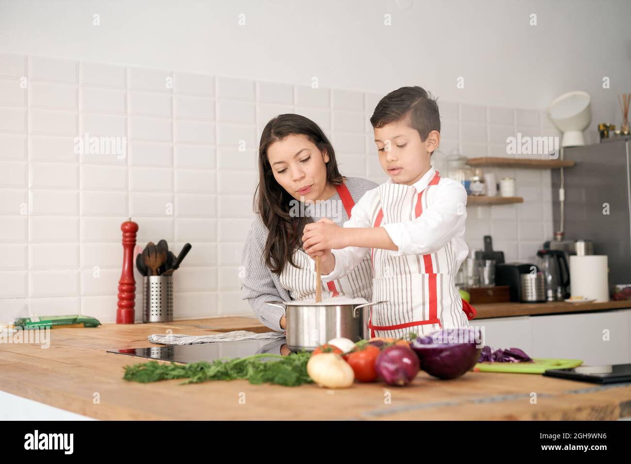 In der Küche: Eine alleinerziehende Familie kocht gemeinsam Pasta. Mutter und Sohn rühren Nudeln im Topf. Kinder helfen Eltern. Gesunde Ernährung. Stockfoto