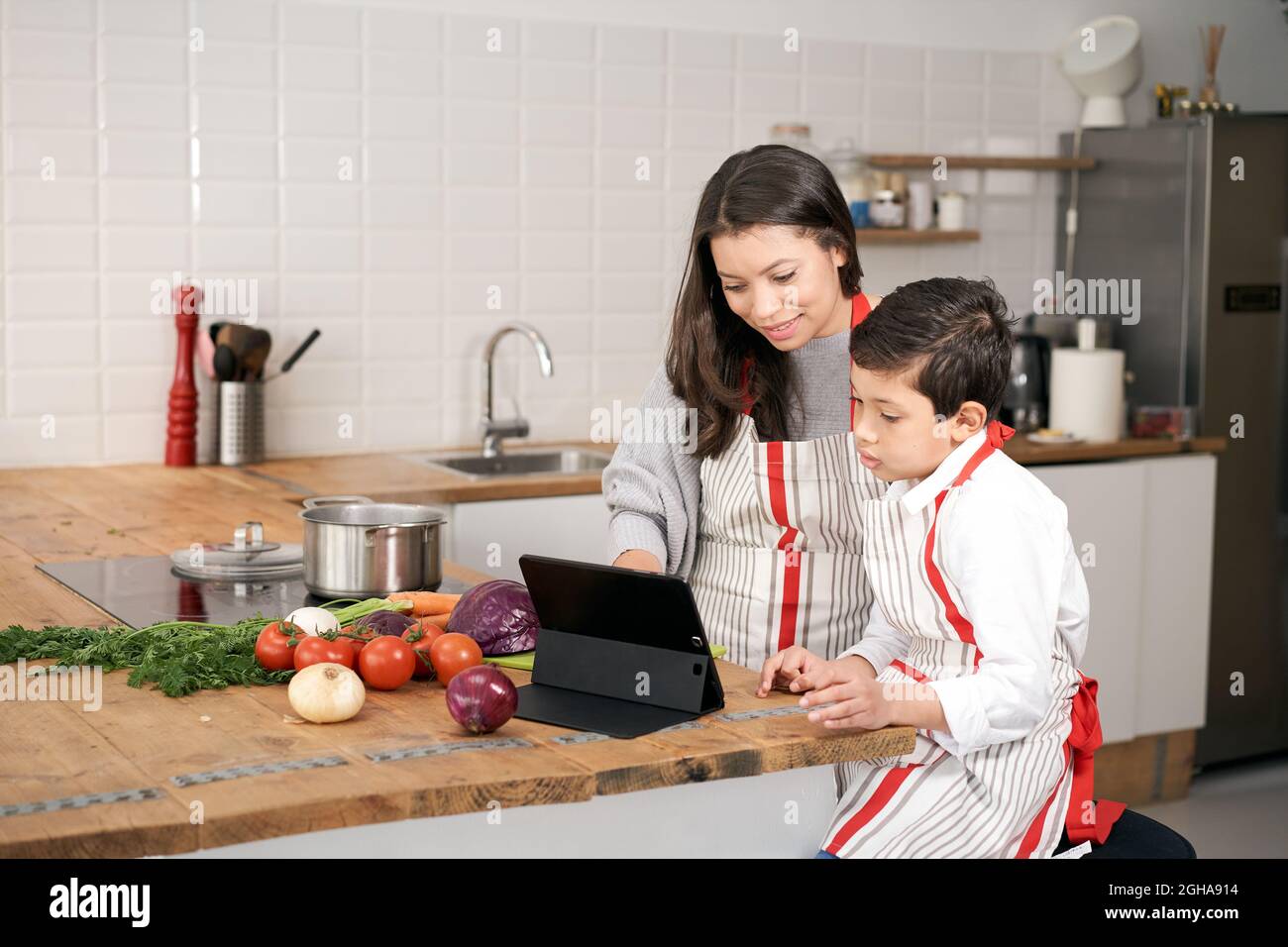 In der Küche: Ein alleinerziehender Familienkoche. Mutter und Sohn suchen über ihr Tablet nach einem Online-Kochrezept. Kinder helfen Eltern Stockfoto