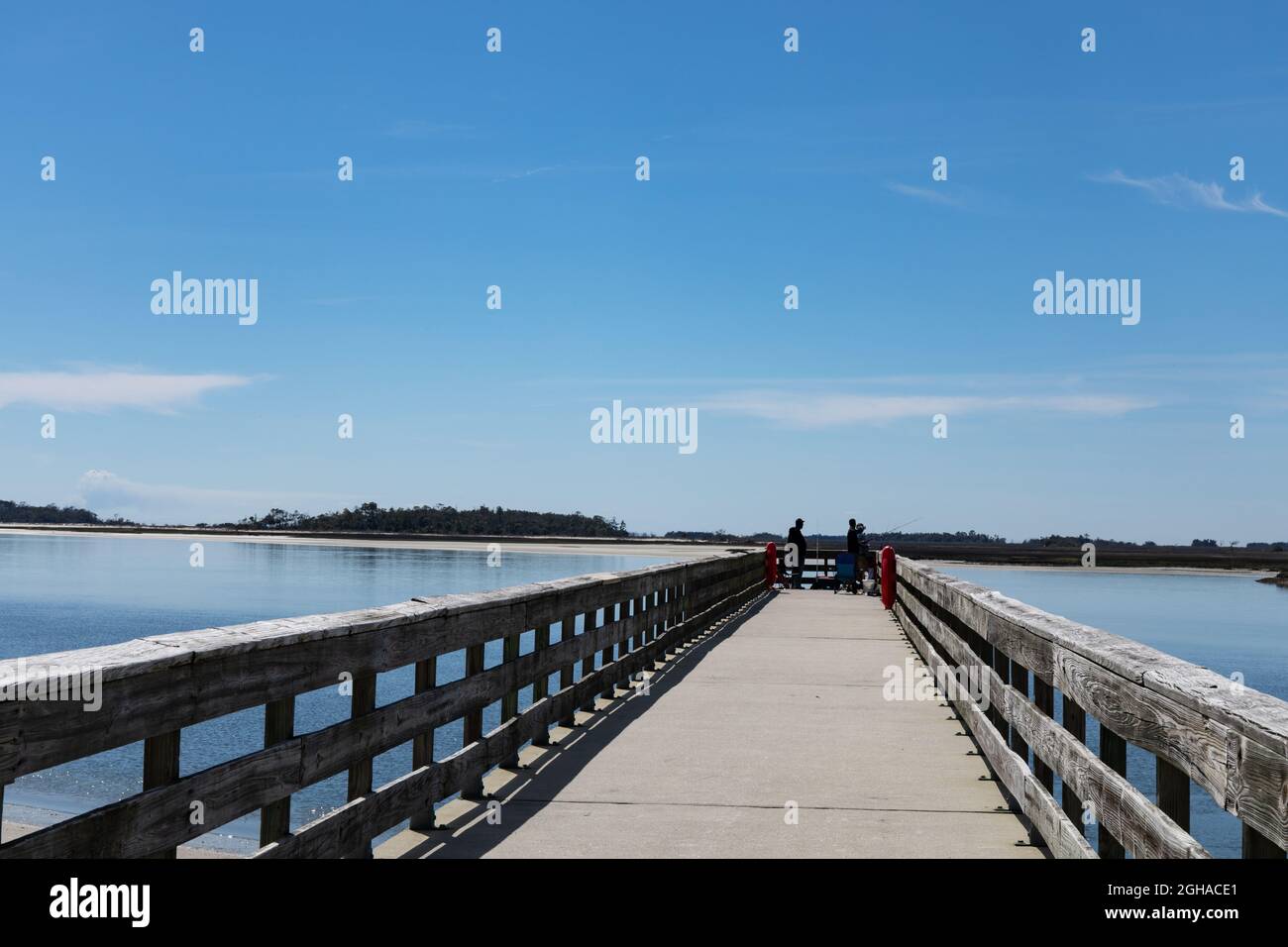Männer fischen am Ende einer langen Pier Promenade auf dem Intracoastal Waterway, schöner blauer Himmel spiegelt sich im Wasser, horizontaler Aspekt Stockfoto
