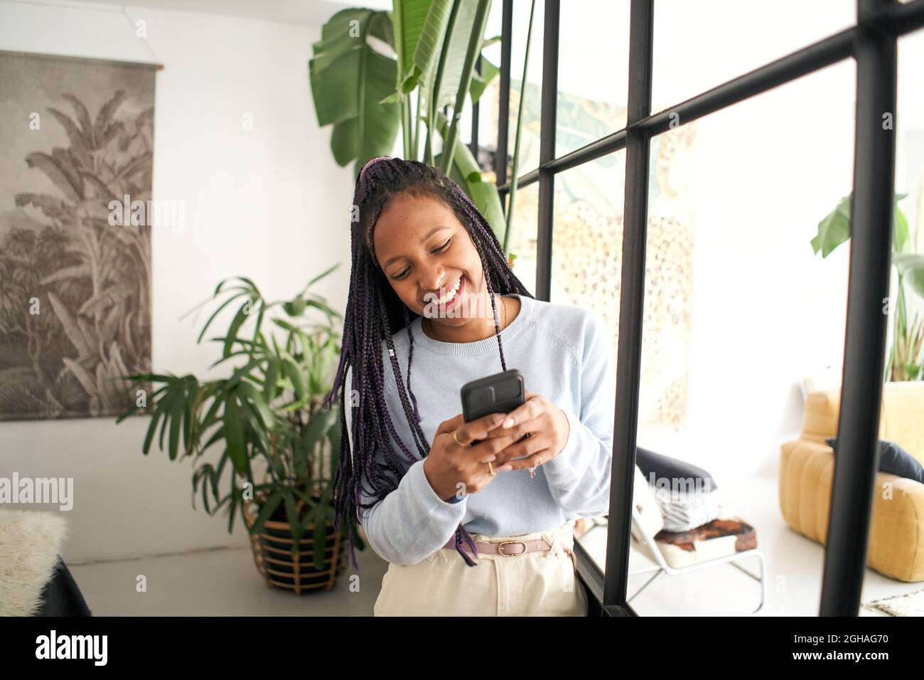 Junge afroamerikanische Frau, die auf ihrem Smartphone chattet. Lächelndes Mädchen, das ein Mobiltelefon in einem modernen Loft benutzt. Stockfoto