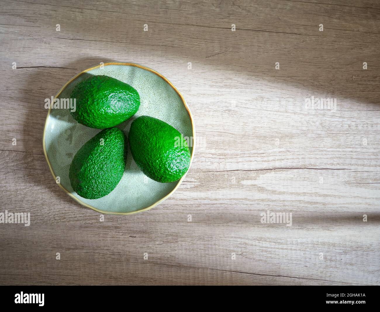 Drei grüne Avocados auf Platte auf Holzfläche Stockfoto