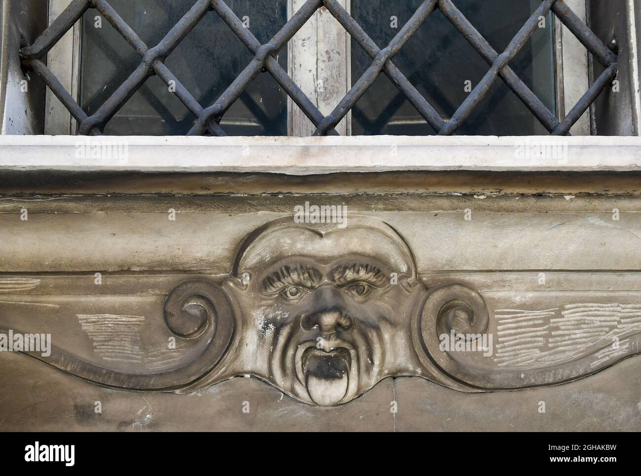 Detail eines alten Gebäudes mit einem Flachrelief, das das verrunzelte Gesicht eines Mannes unter einem Fenster darstellt, das von einem Eisengitter geschlossen wurde, Livorno, Toskana, Italien Stockfoto