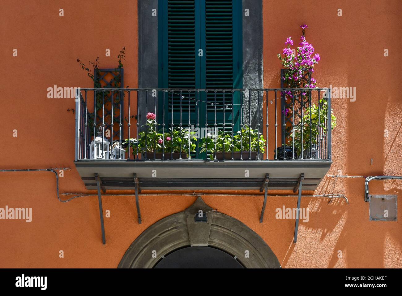 Detail der orangefarbenen façade eines alten Hauses mit blühenden Topfpflanzen auf einem kleinen Balkon im Sommer, Livorno, Toskana, Italien Stockfoto