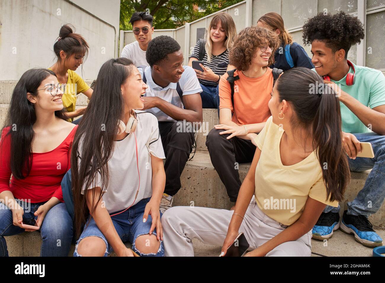 Eine multiethnische Gruppe glücklicher Studenten in einer Pause. Junge Leute lachen auf der Treppe der High School sitzen. Stockfoto