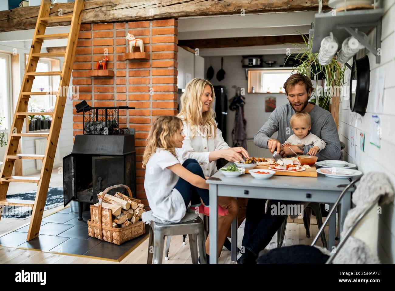 Familie bereitet Pizza zu, während sie zusammen am Tisch zu Hause sitzt Stockfoto