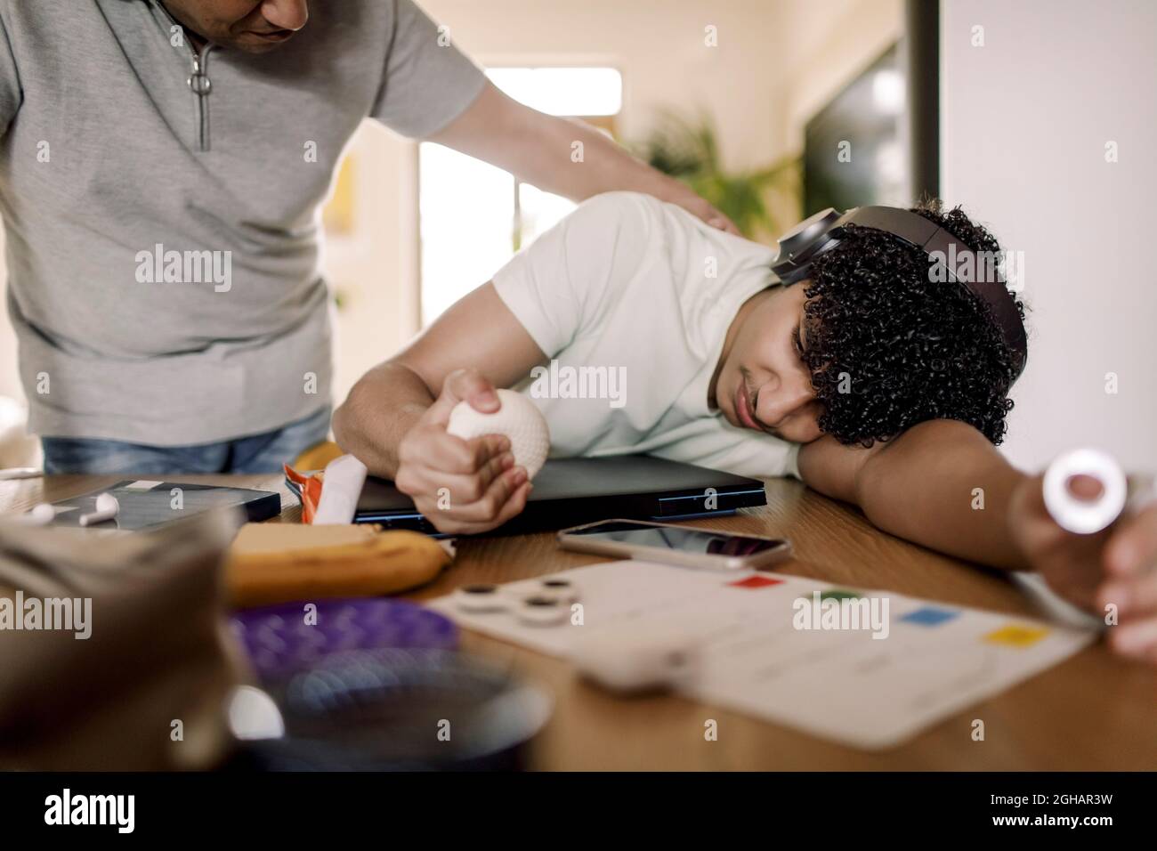 Vater schaut auf den erschöpften Sohn, der zu Hause über dem Tisch liegt Stockfoto