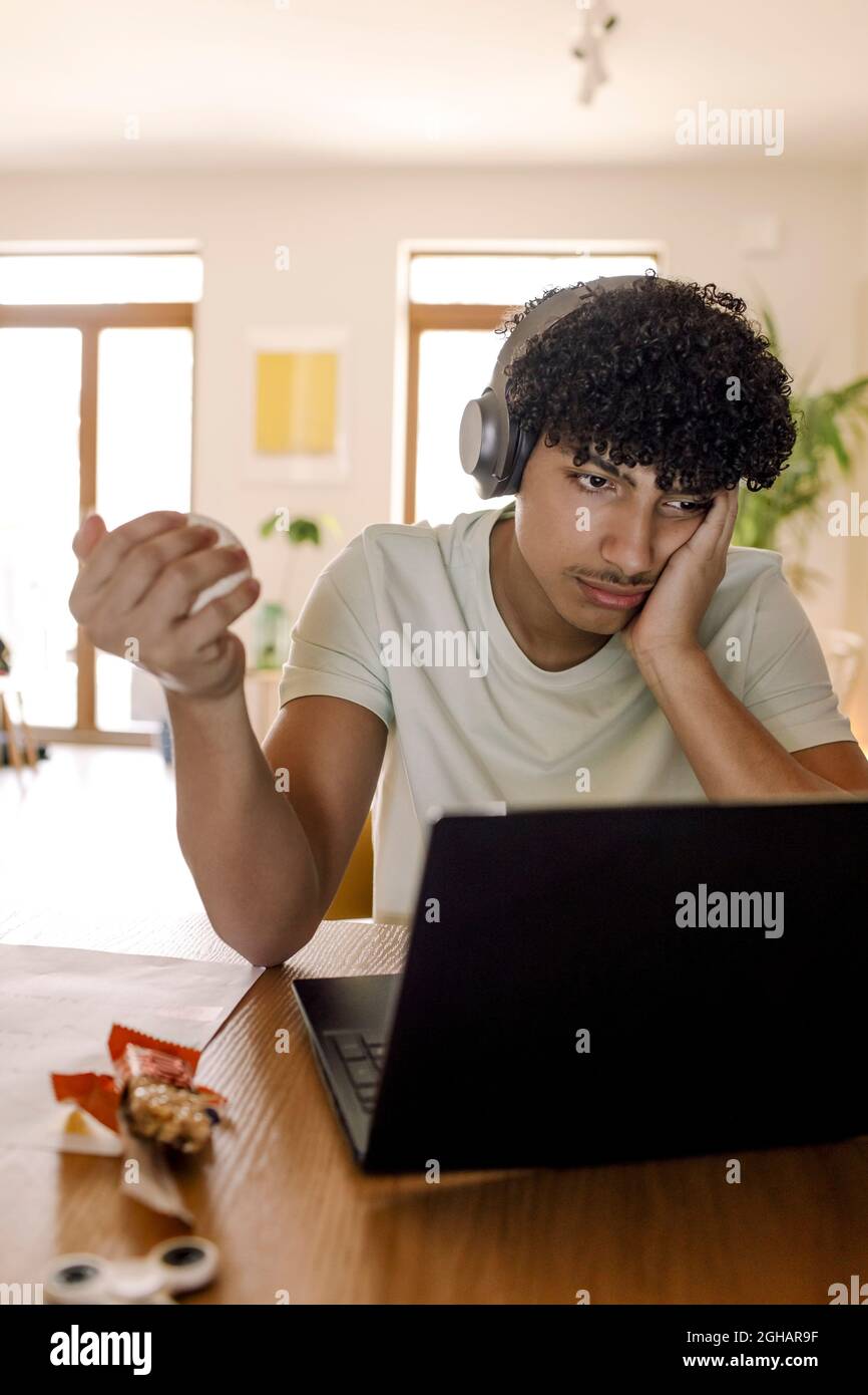 Männlicher Teenager mit Laptop, während er zu Hause sitzt Stockfoto