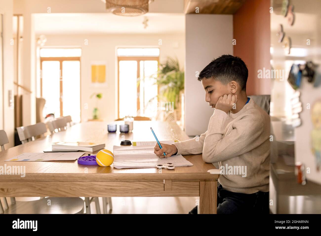 Seitenansicht des Jungen, der zu Hause im Buch über dem Tisch schrieb Stockfoto