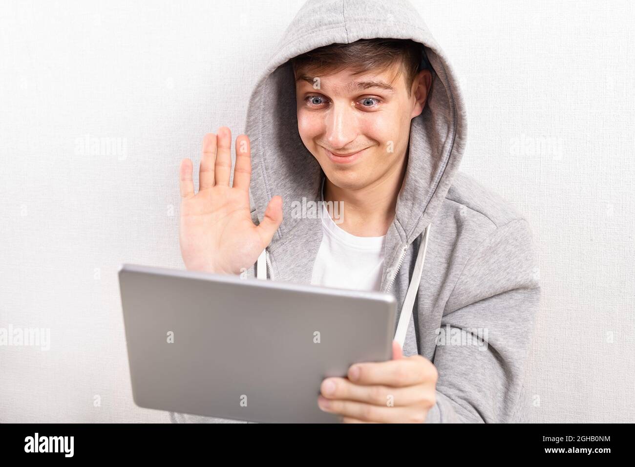 Glücklicher junger Mann mit Tablet-Computer winkt mit der Hand an der weißen Wand Stockfoto