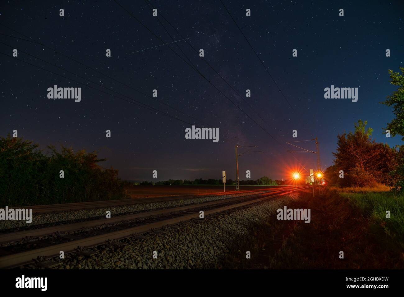 Milkyway mit seinem galaktischen Zentrum über einer einsamen Eisenbahnstrecke, die in einer sternenklaren Nacht über dem Stoppsignal steht. Stockfoto