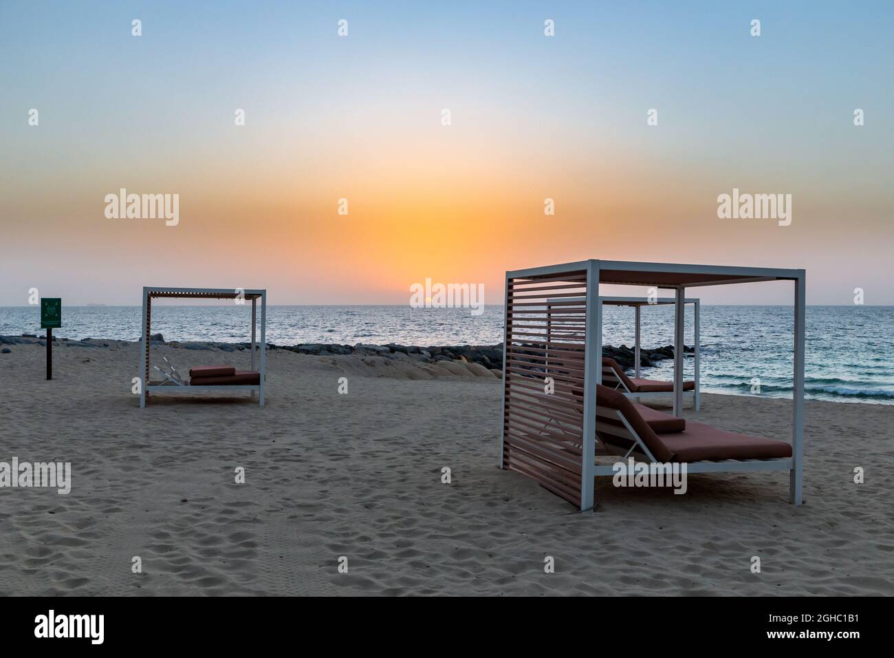 Leerer Sandstrand in Dubai mit doppelten Sonnenliegen, auf der neuen künstlichen Bluewaters Island, keine Menschen aufgrund einer Coronavirus COVID-19 Pandemie, goldener Sonnenuntergang. Stockfoto