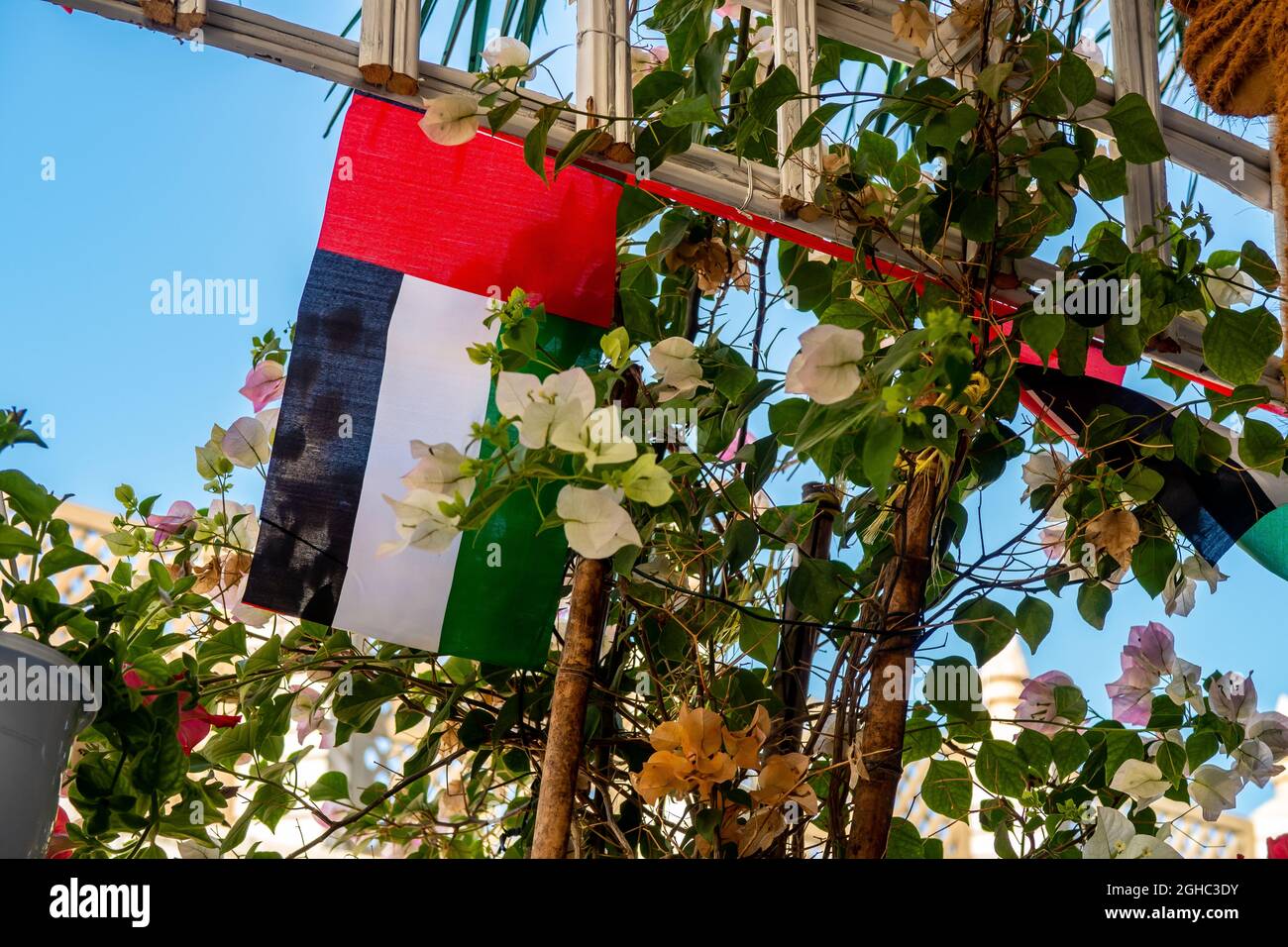 Die Nationalflaggendekorationen der Vereinigten Arabischen Emirate hängen zwischen Blumen, Nationalfeiertag der Vereinigten Arabischen Emirate, Dubai. Stockfoto