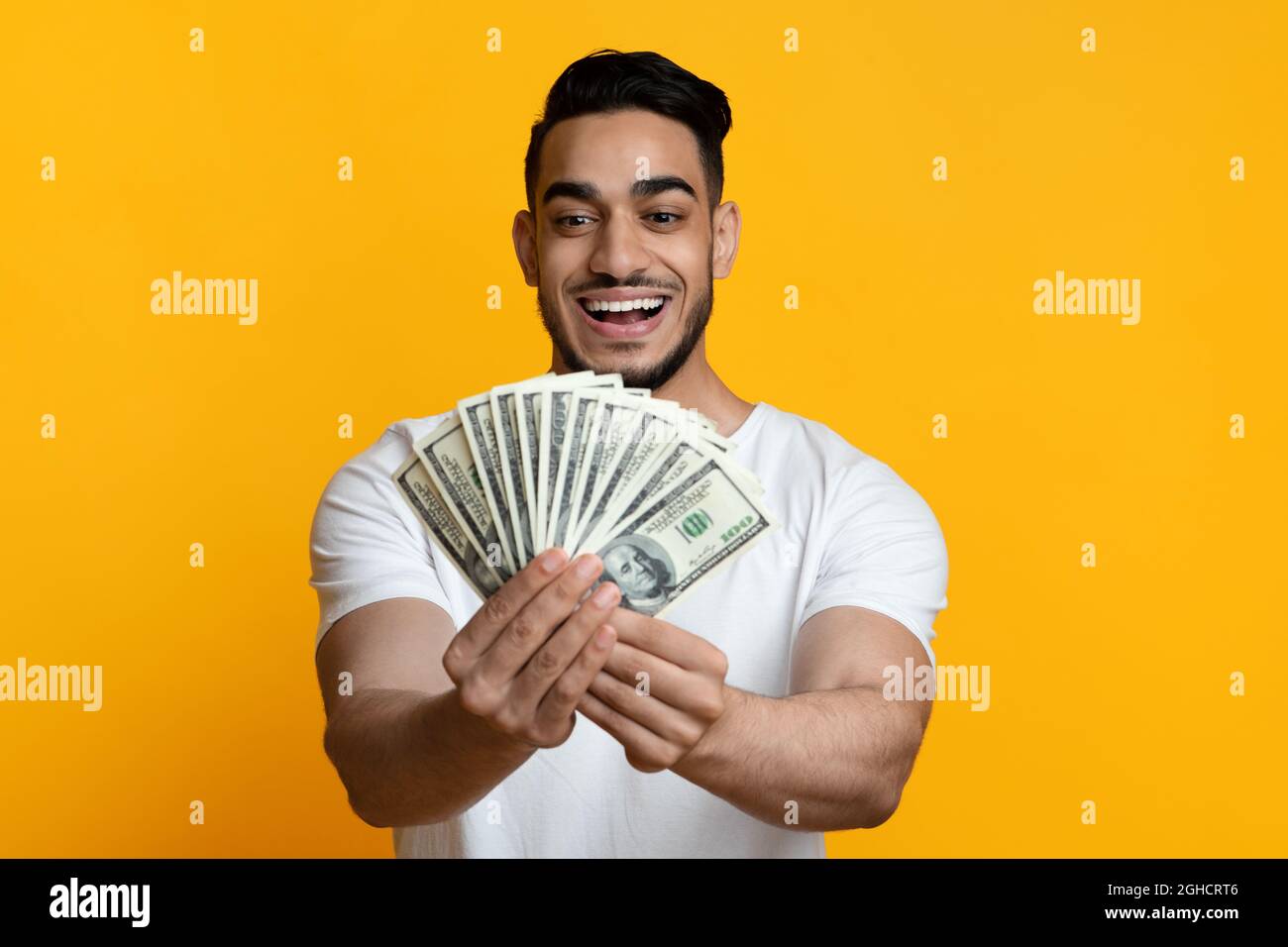 Entzückter Mann aus dem Nahen Osten, der Geld auf gelbem Hintergrund hält Stockfoto