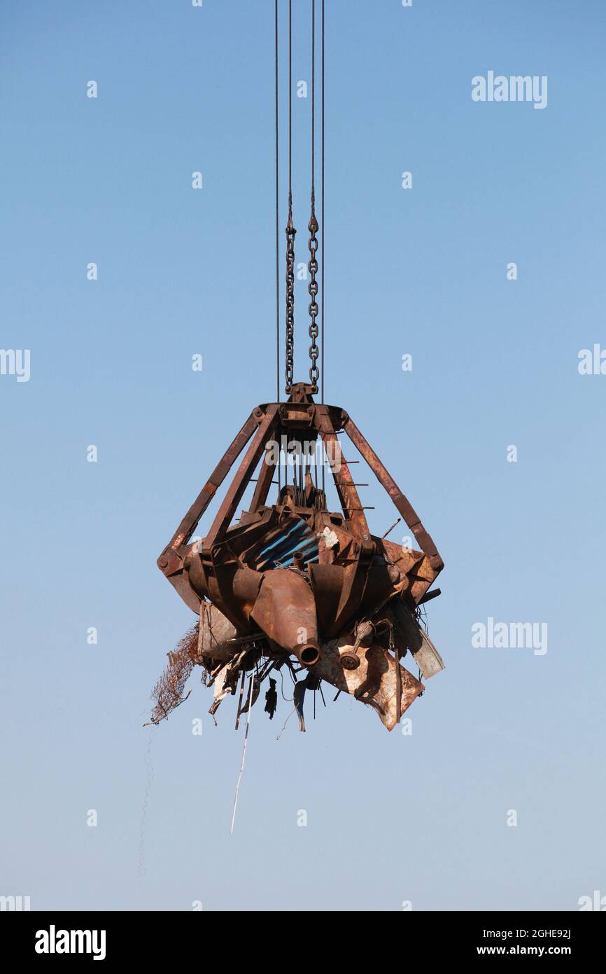 Hydraulischer Greifer eines Hafenkrans, der rostigen Metallschrott zum Recycling transportiert Stockfoto
