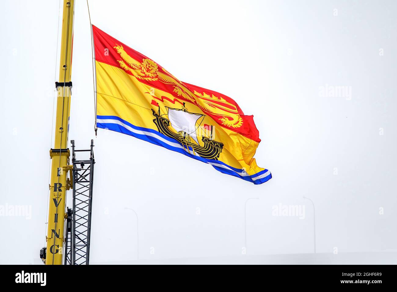 Saint John, NB, Kanada - 14. August 2021: Große Flagge von New Brunswick, die von einem Irving-Kran aus fliegt. Nebliger Tag mit verdeckter Hafenbrücke dahinter. Stockfoto