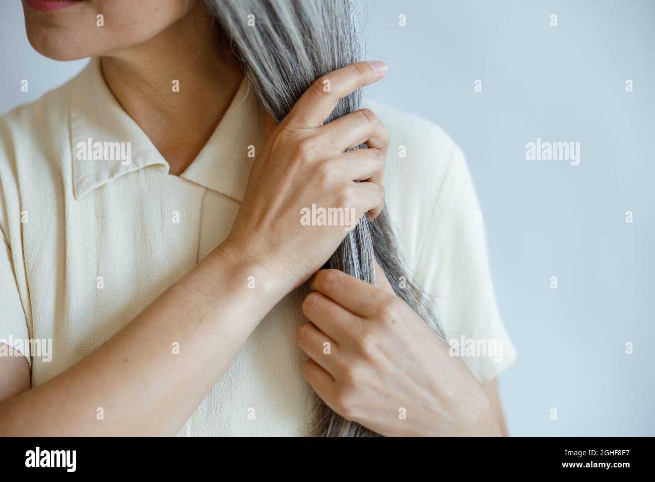 Dame mittleren Alters in eleganter Bluse hält gerade graue Haare Posen auf hellgrauem Hintergrund Stockfoto
