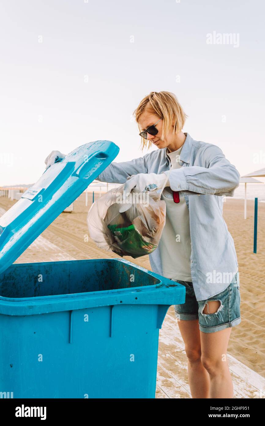 Junge Freiwillige wirft Müllbeutel in den Mülleimer am Strand. Stockfoto
