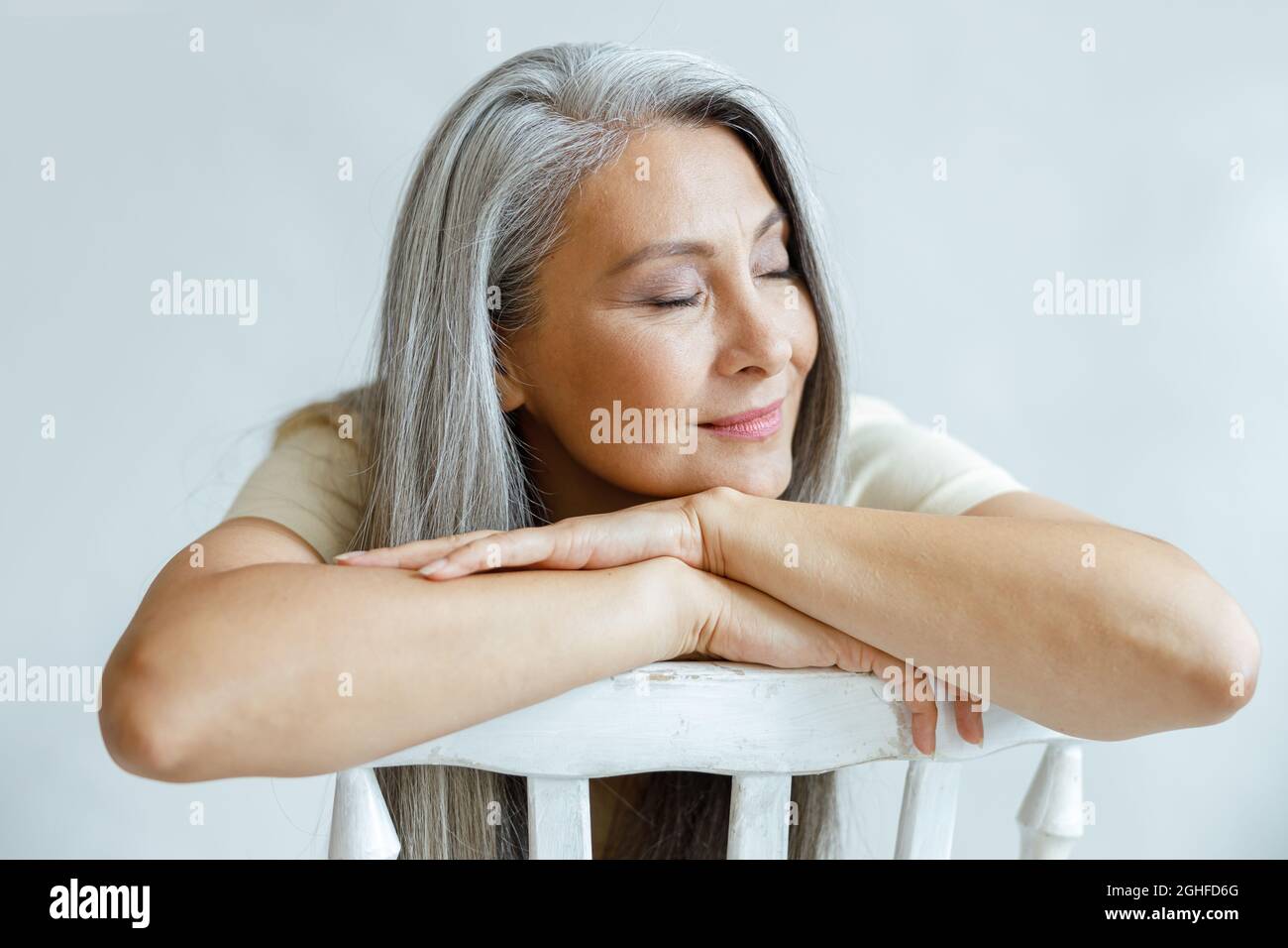 Entspannt silberhaarige asiatische Modell lehnt sich auf den Rücken sitzt rückwärts auf Stuhl im Studio Stockfoto