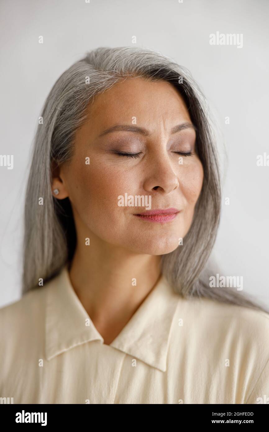 Ruhige Frau mittleren Alters mit geschlossenen Augen steht auf hellem Hintergrund Stockfoto