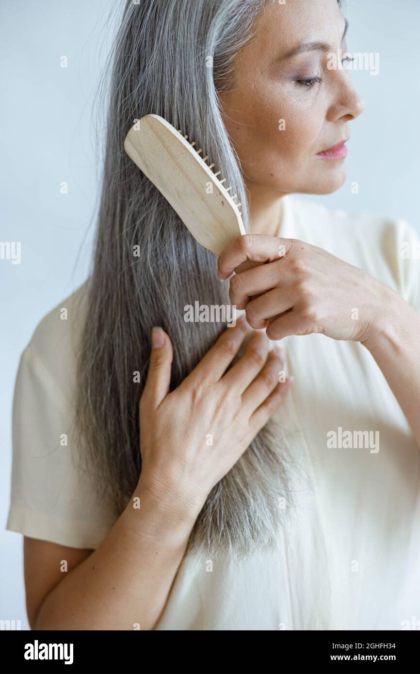 Ruhiges asiatisches Modell mittleren Alters bürstet lange, haarige Haare, die auf hellem Hintergrund posieren Stockfoto