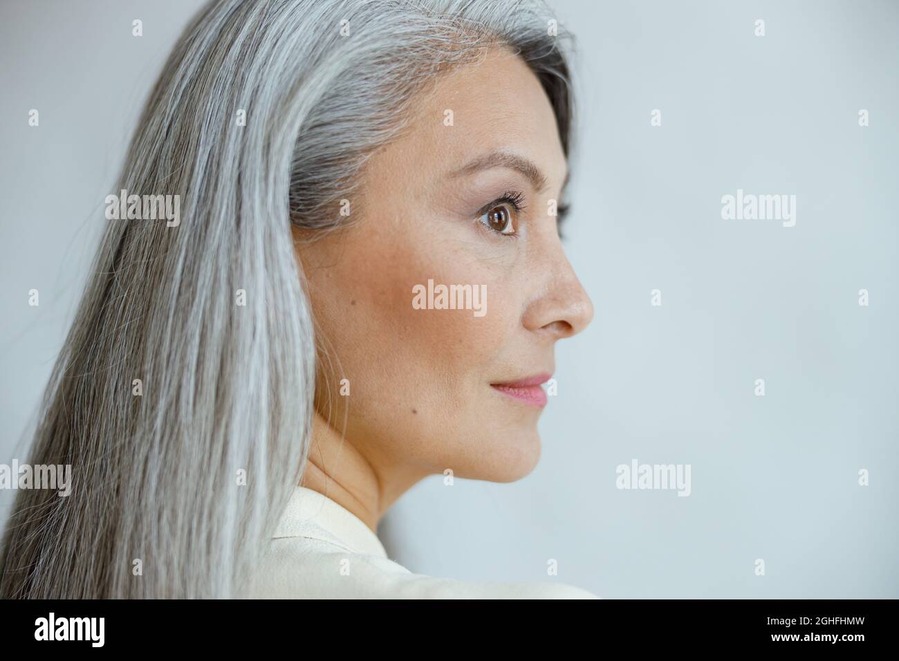 Asiatische Frau mittleren Alters mit schönen geraden Hufhaar auf hellgrauem Hintergrund Stockfoto