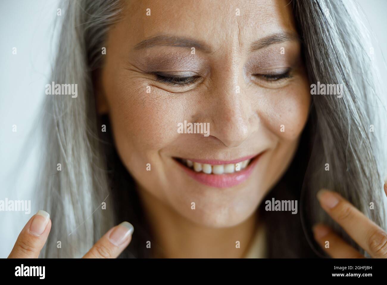 Süßes asiatisches Frauenmodell mittleren Alters mit lockeren grauen Haaren Posen auf hellem Hintergrund Stockfoto
