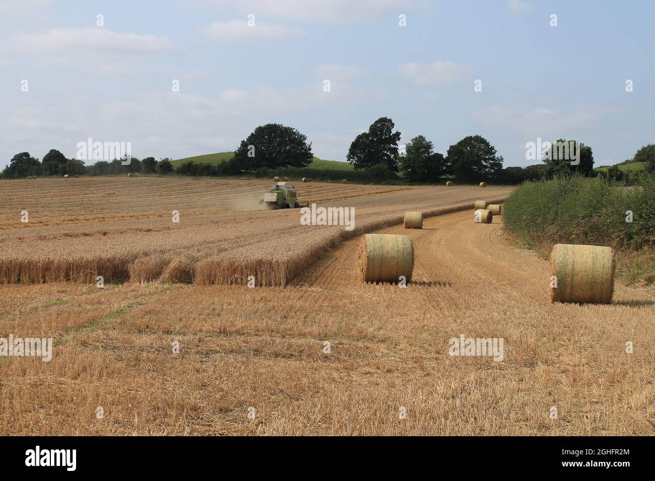 Feld, das am Sommertag in West Yorkshire, Großbritannien, von einem Mähdrescher mit unscharfer Luft und Wolken geerntet wird Stockfoto