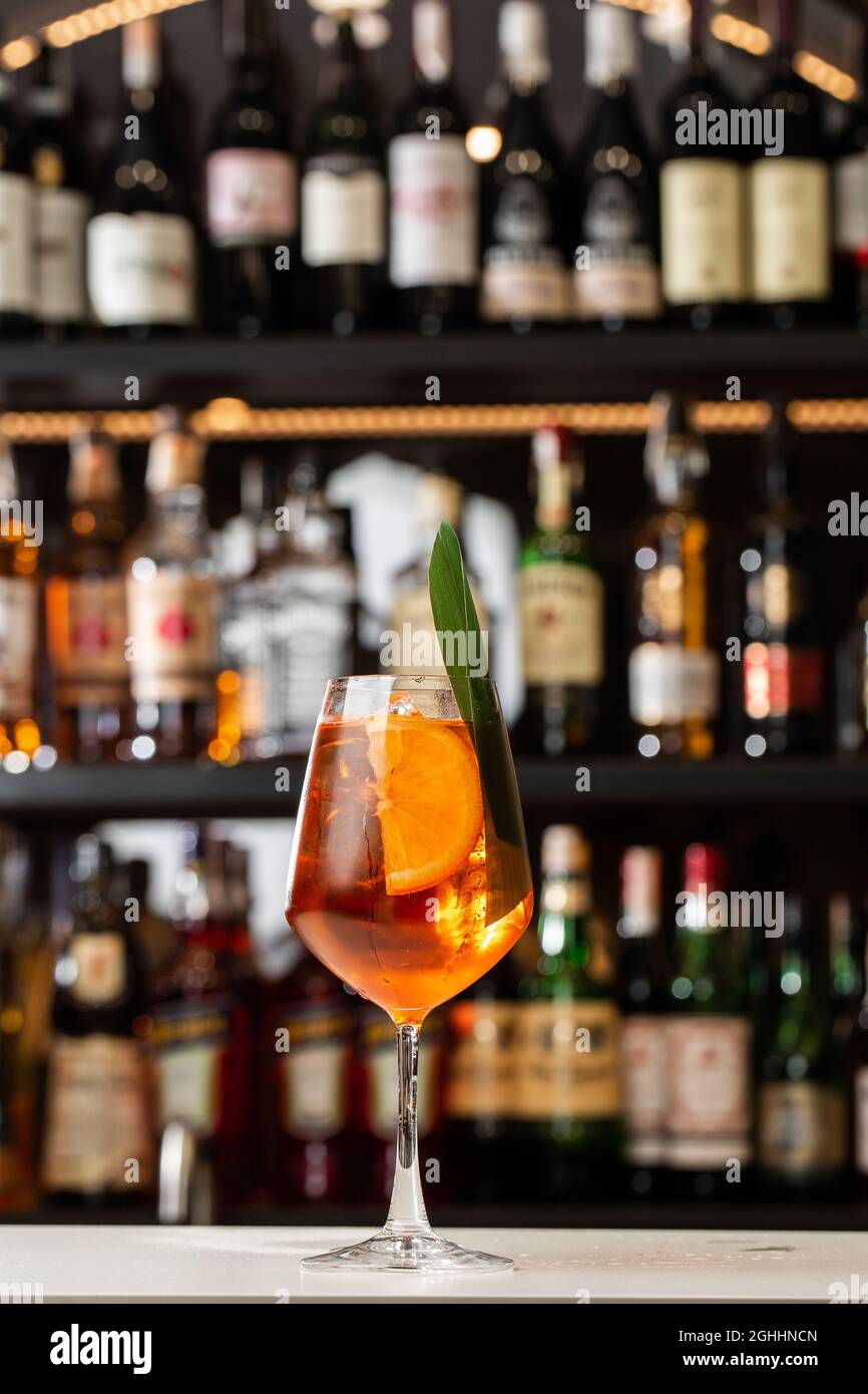Ein Glas eisgekühlter Aperol Spritz-Cocktail, der in einem Weinglas serviert wird, das mit Orangenscheiben und Basilikumblättern verziert ist und auf einer Bar platziert wird Stockfoto