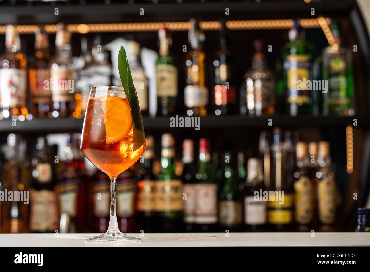 Ein Glas eisgekühlter Aperol Spritz-Cocktail, der in einem Weinglas serviert wird, das mit Orangenscheiben und Basilikumblättern verziert ist und auf einer Bar platziert wird Stockfoto