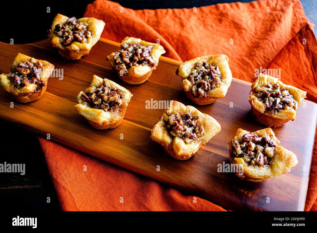 Pecan Pie Tartelettes serviert auf einem Holzschneidebrett: Einzelne Pecan Pie Tarteletten werden auf einem Holzschneidebrett angezeigt Stockfoto